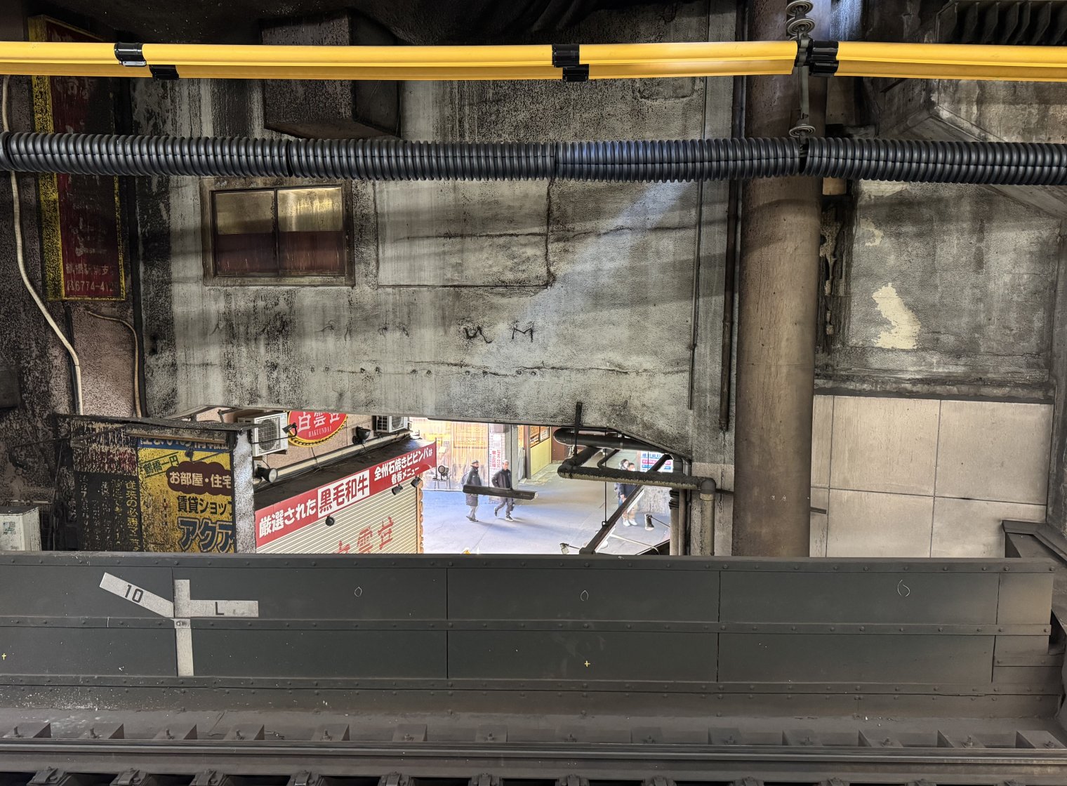 Porthole view of Tsuruhashi Shopping Street from train platform. A restaurant sign likely untouched for at least 50 years hangs coated in train grime.