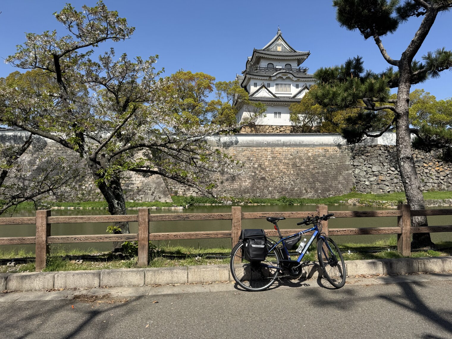 the ever-reliable bicycle, parked in front of Kishiwada Castle, on day 1 of big bike '26. the sky is blue and the castle is japan.